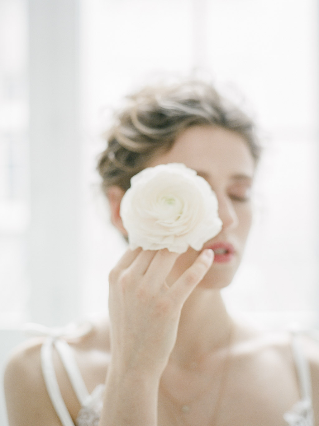 Fine art portrait of a woman in soft light, eyes closed, holding a flower — photographed in Paris studio by Camy Duong.